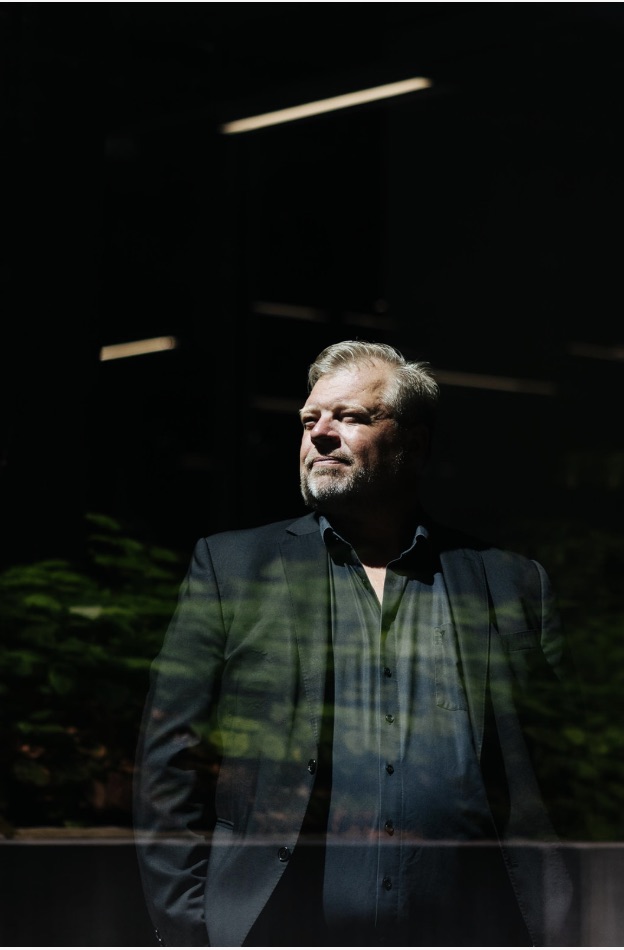 Henrik Stender set gennem en rude med spejlinger af grønt løv